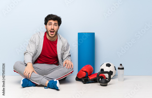 Sport man sitting on the floor with surprise facial expression