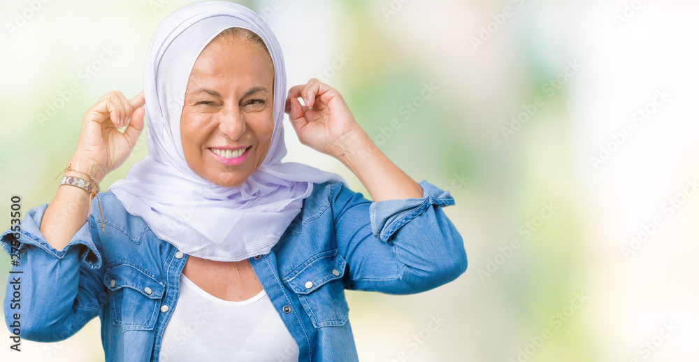 Middle age eastern arab woman wearing arabian hijab over isolated background Smiling pulling ears with fingers, funny gesture. Audition problem