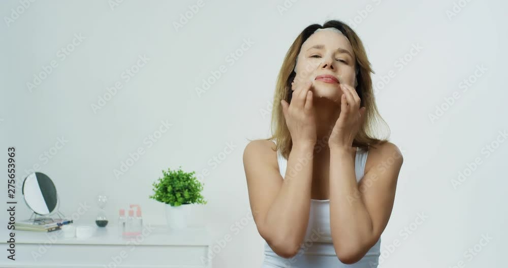 Portrait shot of the Caucasian attractive healthy woman of middle age massaging her face and fighting against wrinkles on the white back wall. Portrait shot of the Caucasian attractive healthy woman of middle age massaging her face and fighting against wrinkles on the white back wall.