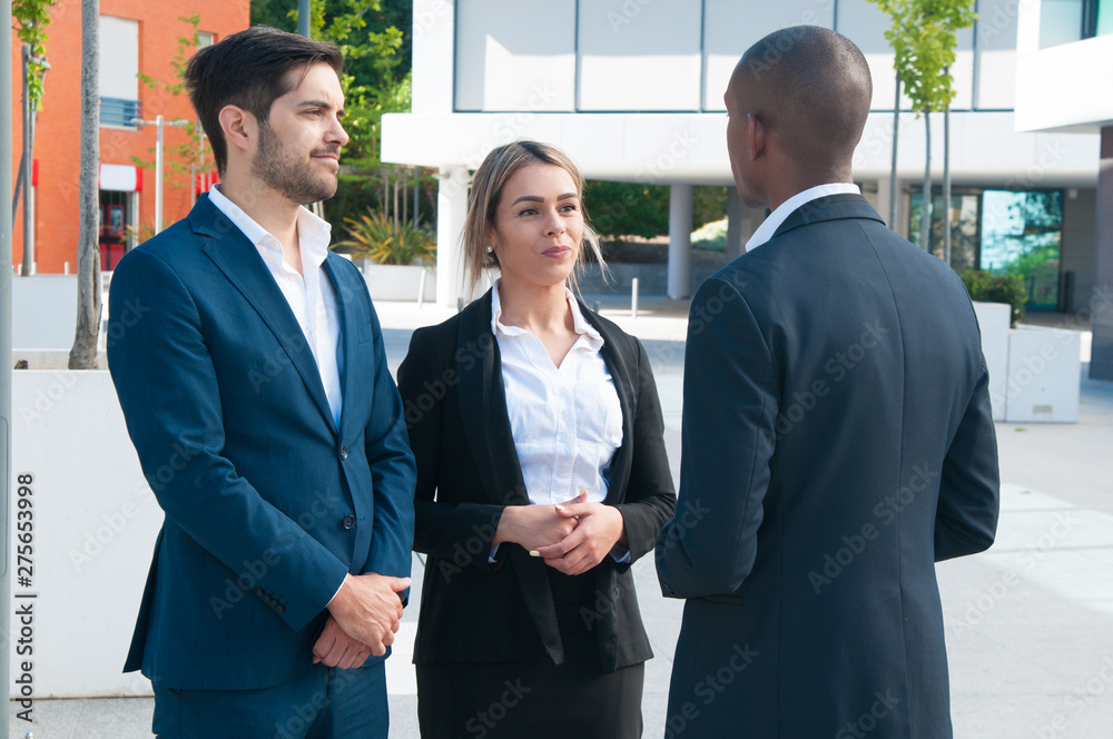 Successful business partners meeting outdoors. Friendly Caucasian man and woman talking to African American business colleague. Negotiation outdoors concept Successful business partners meeting outdoors. Friendly Caucasian man and woman talking to African American business colleague. Negotiation outdoors concept