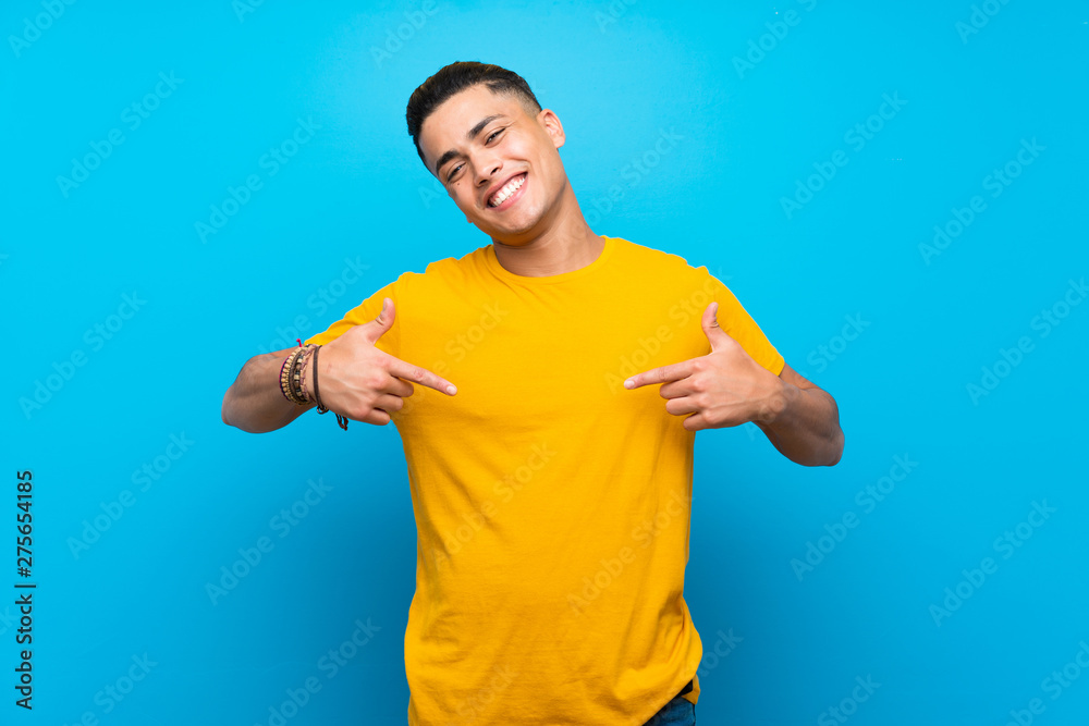 Young man with yellow shirt over isolated blue background proud and self-satisfied Young man with yellow shirt over isolated blue background proud and self-satisfied