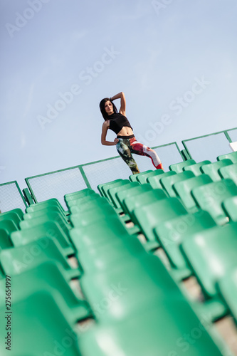 Portrait of a young sports woman leggings and black top near the green and white seats stretcing legs on the stairs before morning jogging in the modern stadium. Healthy lifestyle in the city photo