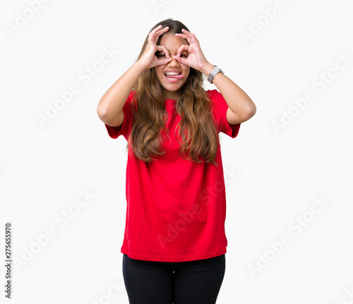 Young beautiful brunette woman wearing red t-shirt over isolated background doing ok gesture like binoculars sticking tongue out, eyes looking through fingers. Crazy expression.