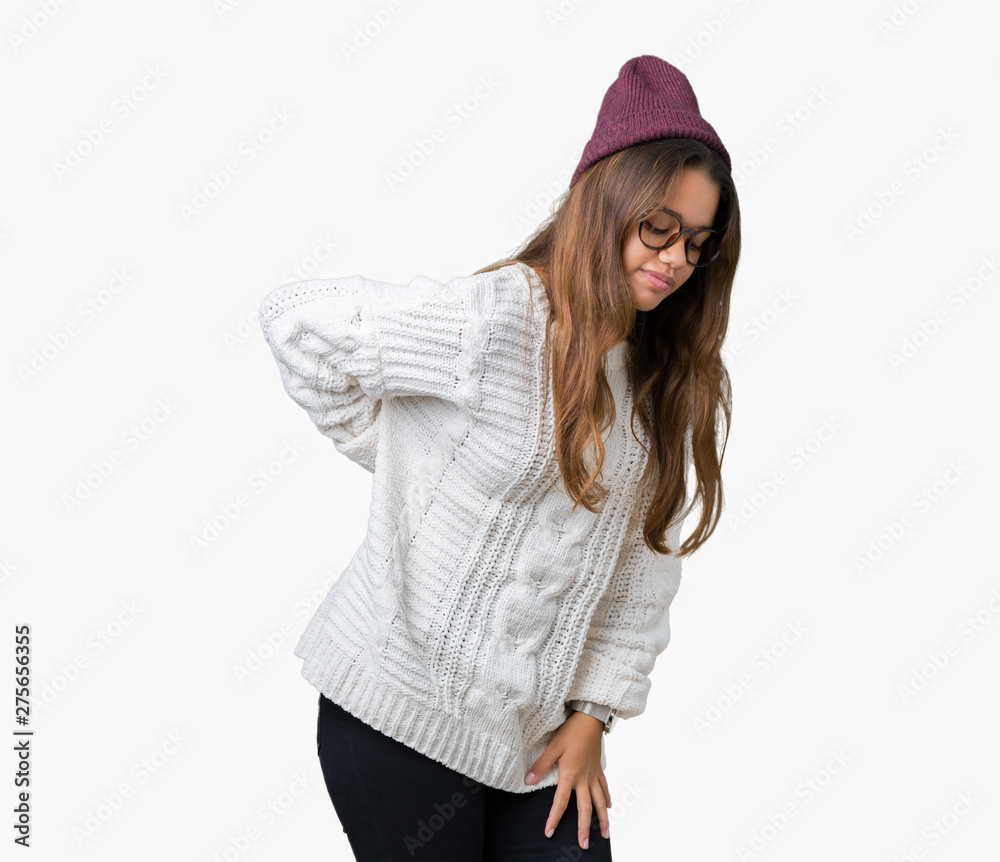 Young beautiful brunette hipster woman wearing glasses and winter hat over isolated background Suffering of backache, touching back with hand, muscular pain Young beautiful brunette hipster woman wearing glasses and winter hat over isolated background Suffering of backache, touching back with hand, muscular pain