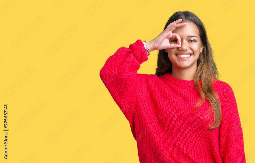 Young beautiful brunette woman wearing red winter sweater over isolated background doing ok gesture with hand smiling, eye looking through fingers with happy face. Young beautiful brunette woman wearing red winter sweater over isolated background doing ok gesture with hand smiling, eye looking through fingers with happy face.