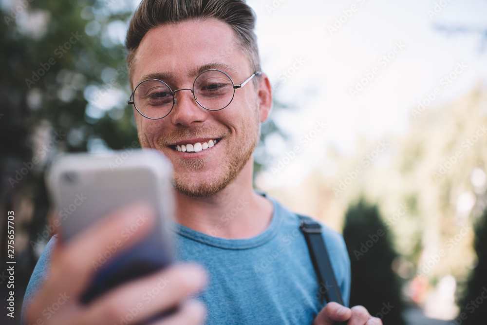 Close up of cheerful Caucasian hipster guy looking at smartphone screen and feeling good from received positive email from friend, happy man in eyewear browsing internet websites via cellular Close up of cheerful Caucasian hipster guy looking at smartphone screen and feeling good from received positive email from friend, happy man in eyewear browsing internet websites via cellular