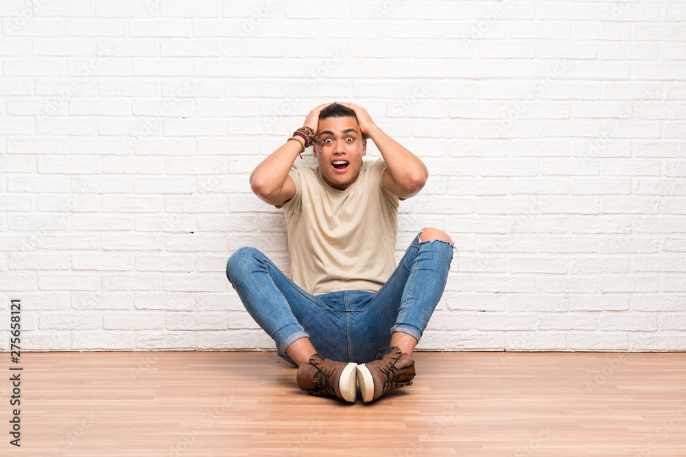 Young man sitting on the floor with surprise facial expression
