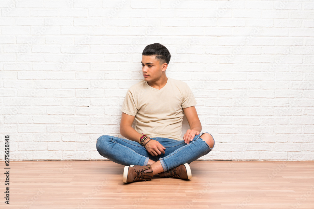 Young man sitting on the floor looking side Young man sitting on the floor looking side