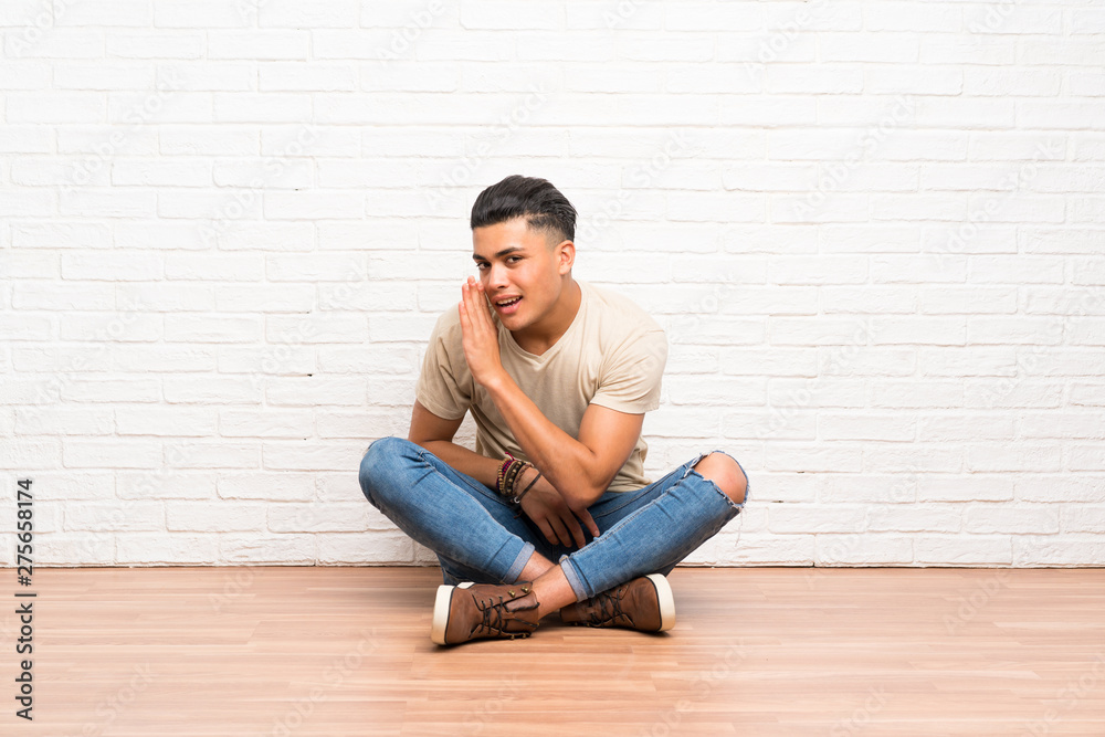 Young man sitting on the floor whispering something Young man sitting on the floor whispering something