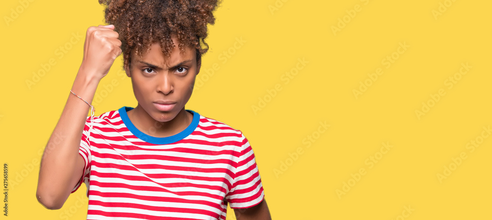 Beautiful young african american woman over isolated background angry and mad raising fist frustrated and furious while shouting with anger. Rage and aggressive concept. Beautiful young african american woman over isolated background angry and mad raising fist frustrated and furious while shouting with anger. Rage and aggressive concept.