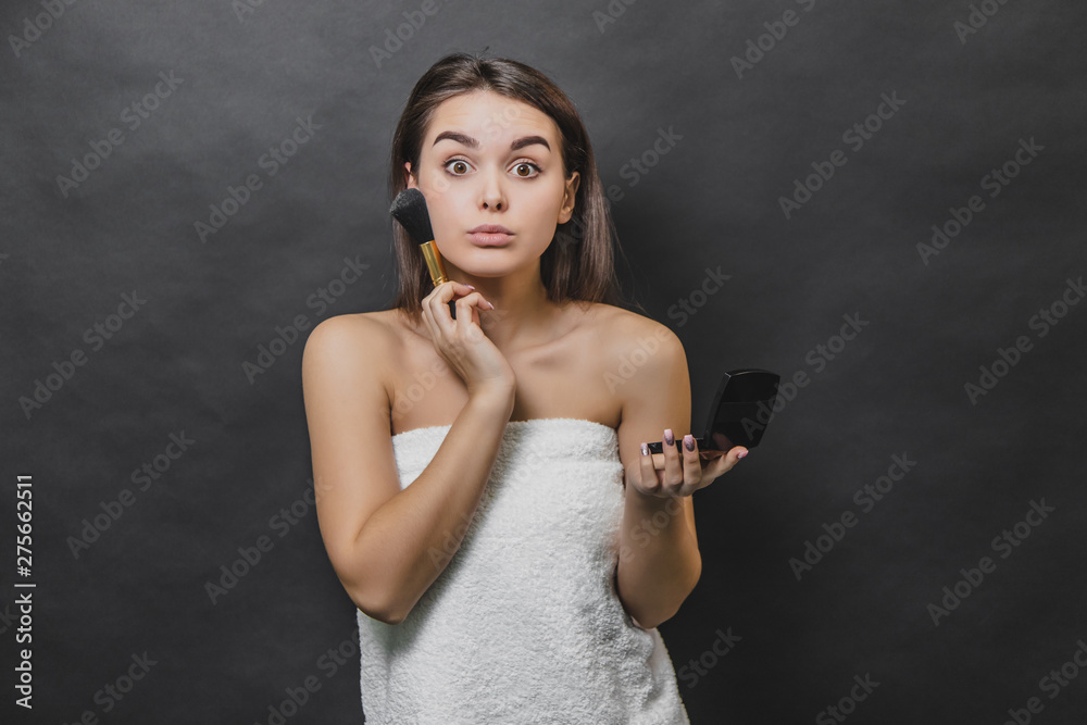 Obraz premium Surprised gorgeous girl with long hair posing, using makeup brush for applying blush.
