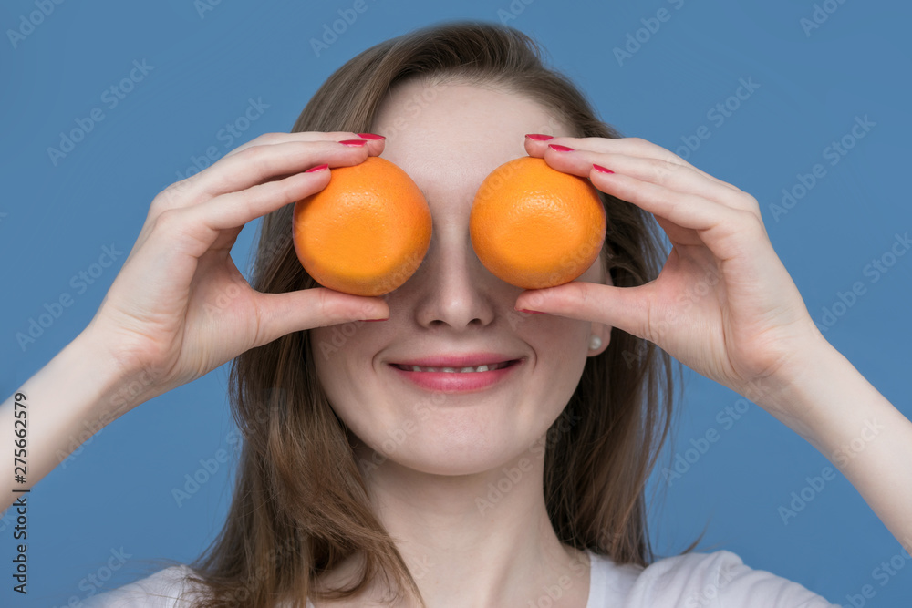 Young beautiful girl model with oranges on blue background, holding oranges between eyes, close up Young beautiful girl model with oranges on blue background, holding oranges between eyes, close up