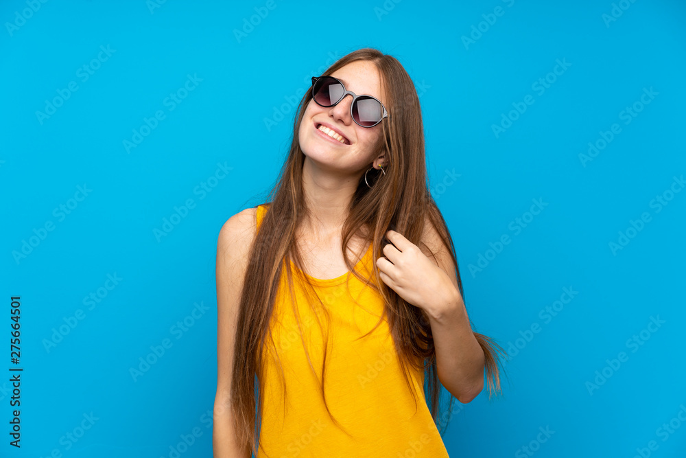 Young woman with long hair over isolated blue wall with glasses and happy