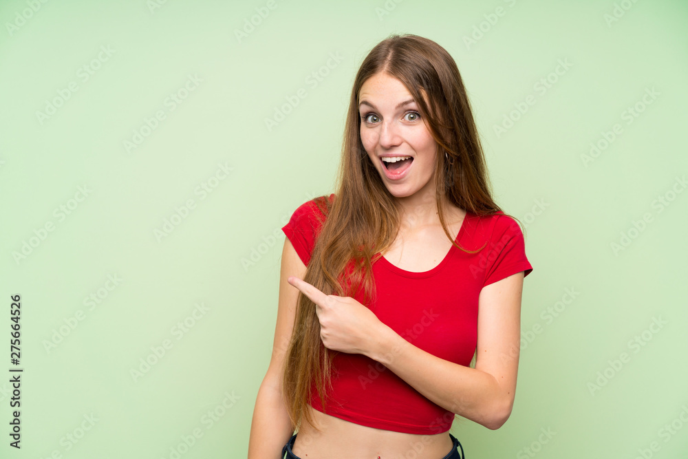 Young woman with long hair over isolated green wall pointing finger to the side
