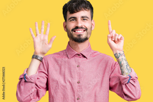 Young handsome man wearing pink shirt over isolated background showing and pointing up with fingers number six while smiling confident and happy. © Krakenimages.com