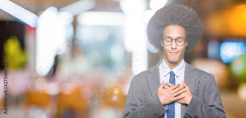 Young african american business man with afro hair wearing glasses smiling with hands on chest with closed eyes and grateful gesture on face. Health concept.