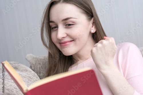 The woman is delighted with reading the book, beautiful girl sitting at home on the couch, reading a book, close up