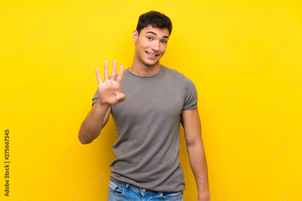 Handsome man over isolated yellow wall happy and counting four with fingers Handsome man over isolated yellow wall happy and counting four with fingers