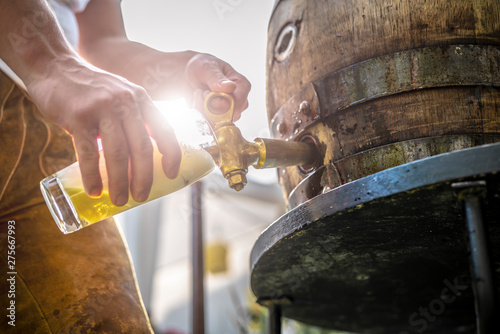 Foto bayerischer Mann in Lederhose sticht ein Holzfass Bier im Garten an und genießt