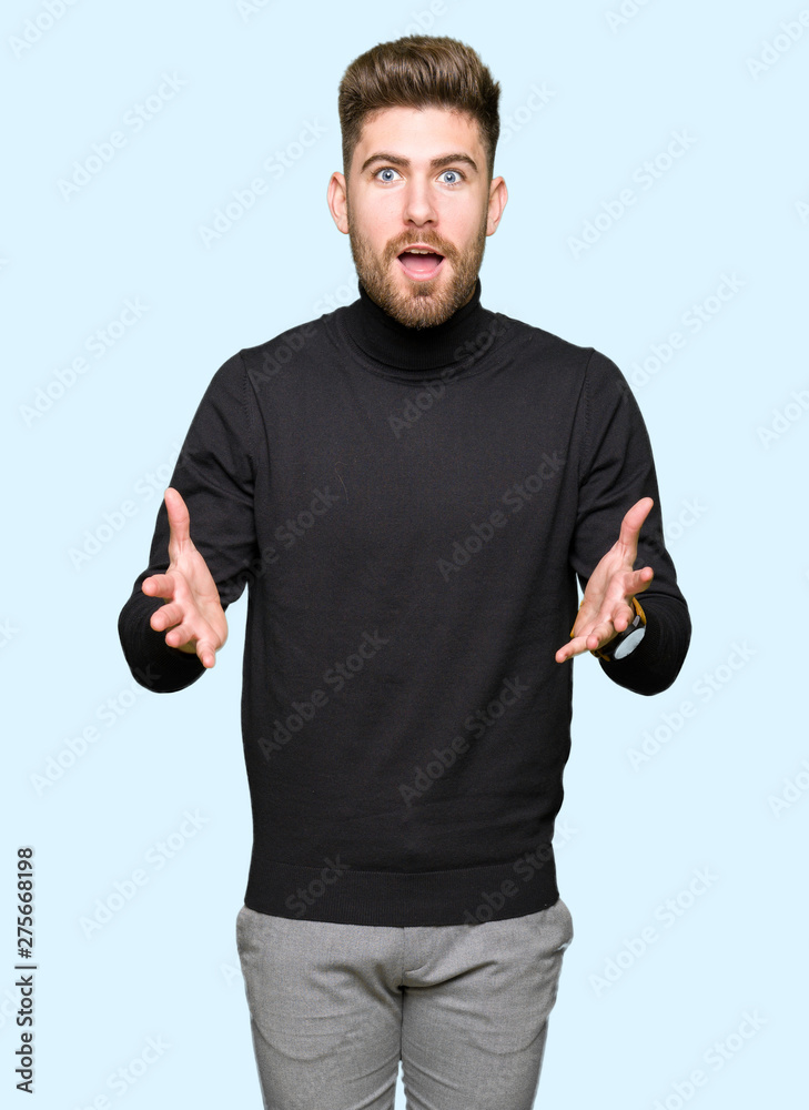 Fototapeta premium Young handsome blond man wearing winter sweater afraid and shocked with surprise expression, fear and excited face.