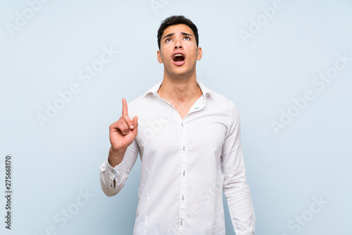 Handsome man over blue wall pointing up and surprised