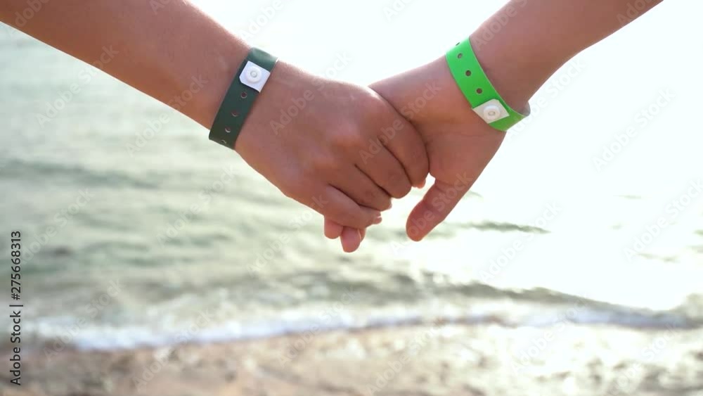 Closeup view of child and mother holding hands happy to stand at seashore during summer beach vacations. Wrists with green bands of hotel resort or amusement park. Closeup view of child and mother holding hands happy to stand at seashore during summer beach vacations. Wrists with green bands of hotel resort or amusement park.