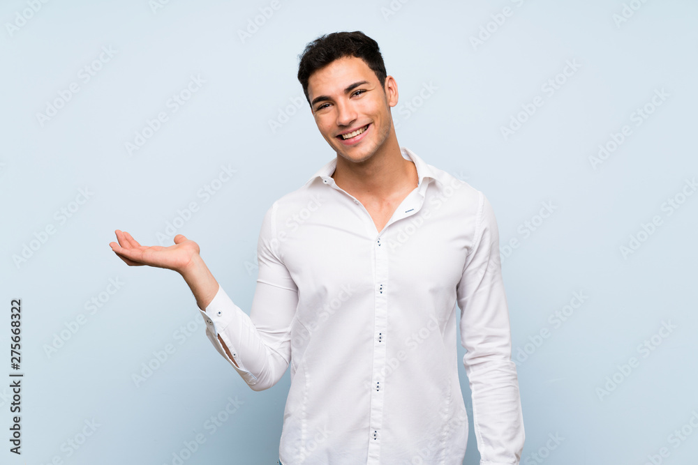 Handsome man over blue wall holding copyspace imaginary on the palm to insert an ad Handsome man over blue wall holding copyspace imaginary on the palm to insert an ad