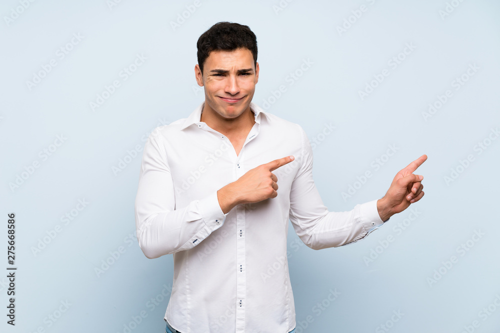 Handsome man over blue wall frightened and pointing to the side Handsome man over blue wall frightened and pointing to the side