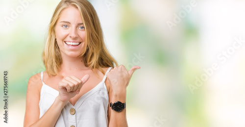 Beautiful young woman over isolated background Pointing to the back behind with hand and thumbs up, smiling confident photo