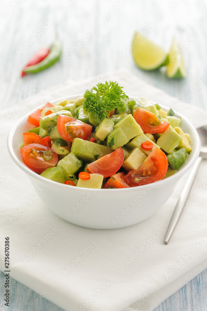 Salsa from avocado, cherry tomatoes and lime. Traditional salad from fresh vegetables with avocado. A serving is serialized in a deep white bowl on a white napkin. Salsa from avocado, cherry tomatoes and lime. Traditional salad from fresh vegetables with avocado. A serving is serialized in a deep white bowl on a white napkin.