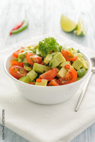 Salsa from avocado, cherry tomatoes and lime. Traditional salad from fresh vegetables with avocado. A serving is serialized in a deep white bowl on a white napkin.