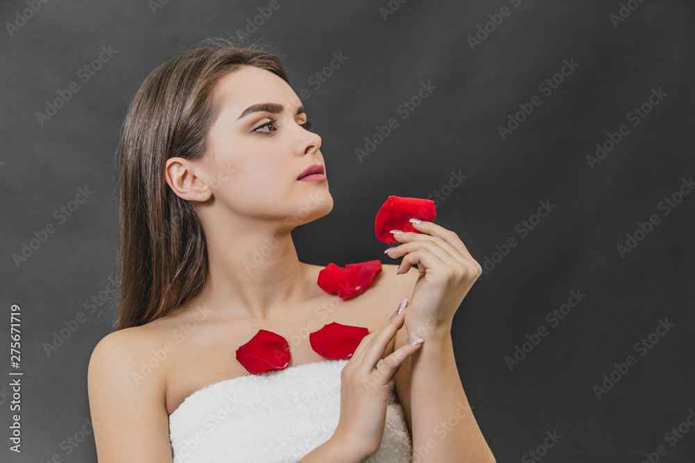 Beautiful young girl stands on a black background. During this time in the spa salon after the procedures on the body has a petal of red rose. Beautiful young girl stands on a black background. During this time in the spa salon after the procedures on the body has a petal of red rose.