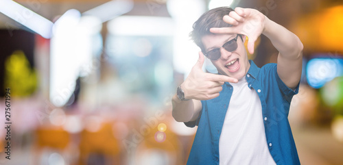 Young handsome man wearing sunglasses over isolated background smiling making frame with hands and fingers with happy face. Creativity and photography concept.