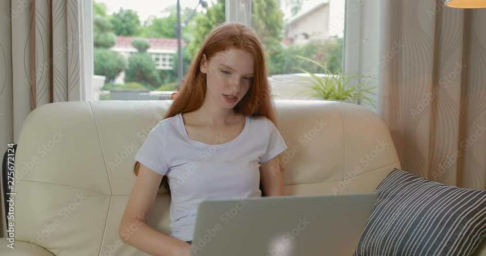 Attractive girl sitting at home on the couch uses modern laptop. tracking shot. in slow motion. Shot on Canon 1DX mark2 4K camera Attractive girl sitting at home on the couch uses modern laptop. tracking shot. in slow motion. Shot on Canon 1DX mark2 4K camera