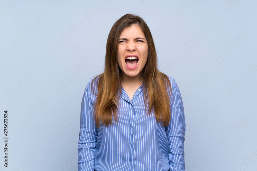 Young girl over isolated blue wall shouting to the front with mouth wide open Young girl over isolated blue wall shouting to the front with mouth wide open