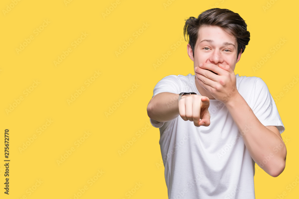 Young handsome man wearing casual white t-shirt over isolated background Laughing of you, pointing to the camera with finger hand over mouth, shame expression Young handsome man wearing casual white t-shirt over isolated background Laughing of you, pointing to the camera with finger hand over mouth, shame expression
