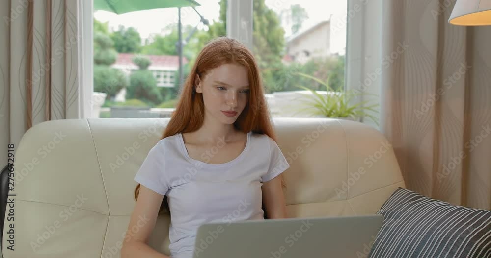 Attractive girl sitting at home on the couch uses modern laptop. tracking shot. in slow motion. Shot on Canon 1DX mark2 4K camera Attractive girl sitting at home on the couch uses modern laptop. tracking shot. in slow motion. Shot on Canon 1DX mark2 4K camera