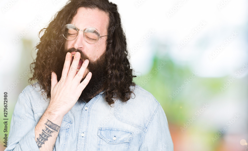 Young hipster man with long hair and beard wearing glasses bored yawning tired covering mouth with hand. Restless and sleepiness. Young hipster man with long hair and beard wearing glasses bored yawning tired covering mouth with hand. Restless and sleepiness.