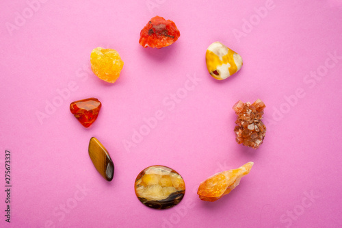 A circle of different minerals on pink background. Spiritual amber, calcite, Aragonite, Simbercite, Jasper, Tiger's eye minerals on flat lay copyspace