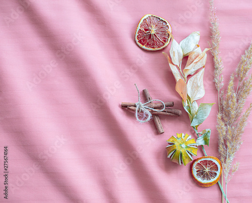 Dried oranges, cinnamon and herbs against a pink fabric background photo