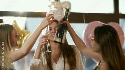 Medium slow motion handheld shot of tipsy girlfriends celebrating with champagne at house party, with shiny balloons in background