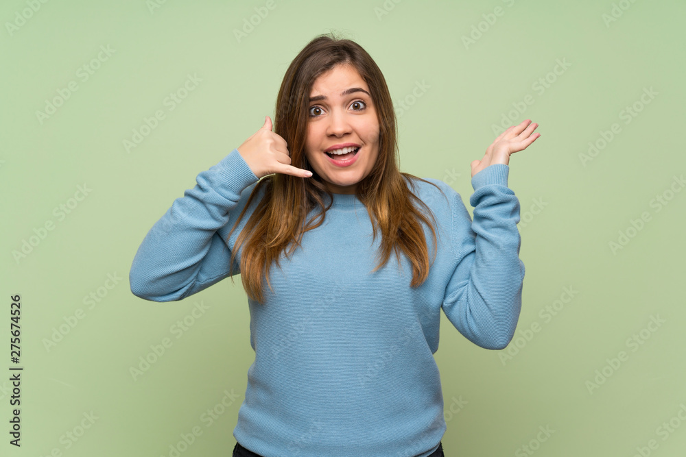 Young girl over green wall making phone gesture and doubting Young girl over green wall making phone gesture and doubting