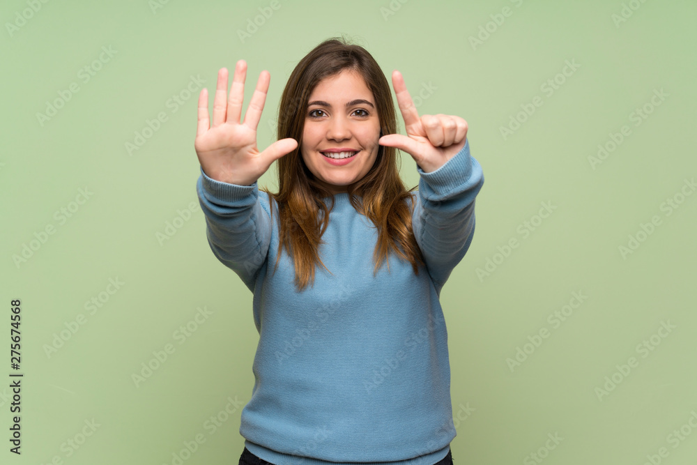 Fototapeta premium Young girl over green wall counting seven with fingers