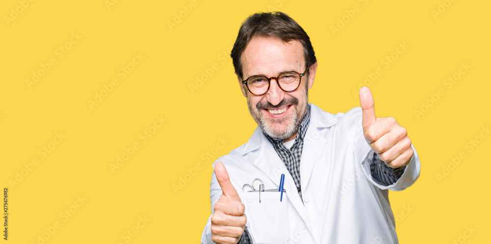 Middle age doctor men wearing medical coat approving doing positive gesture with hand, thumbs up smiling and happy for success. Looking at the camera, winner gesture.