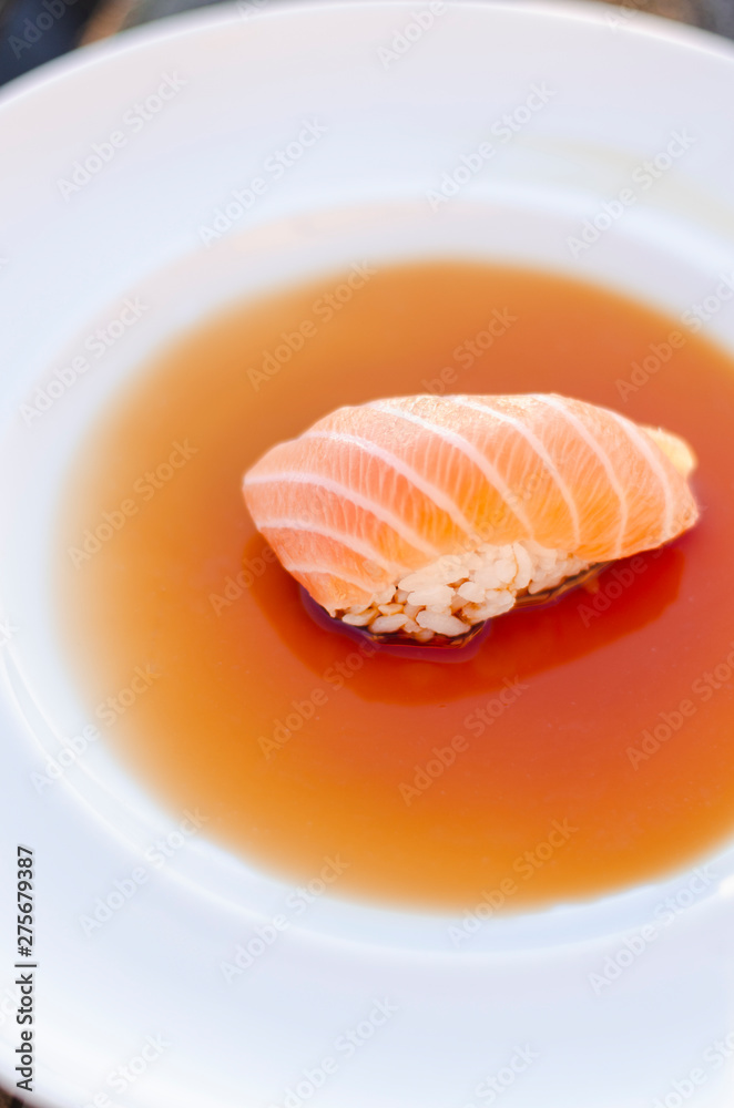 A nigiri sushi with salmon in soy sauce on white plate. A nigiri sushi with salmon in soy sauce on white plate.