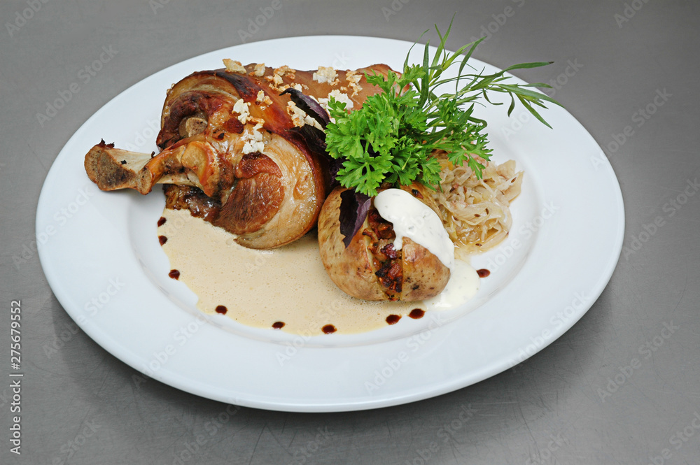 Roasted pork knuckle with stewed cabbage and vegetables on plate, on gray background