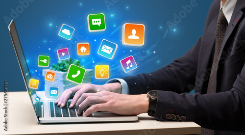 Businessman hand typing on laptop with flying application icons around 