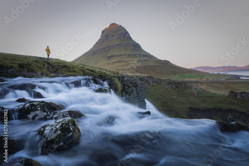 a person standing on the edge by waterfall watching the mountain