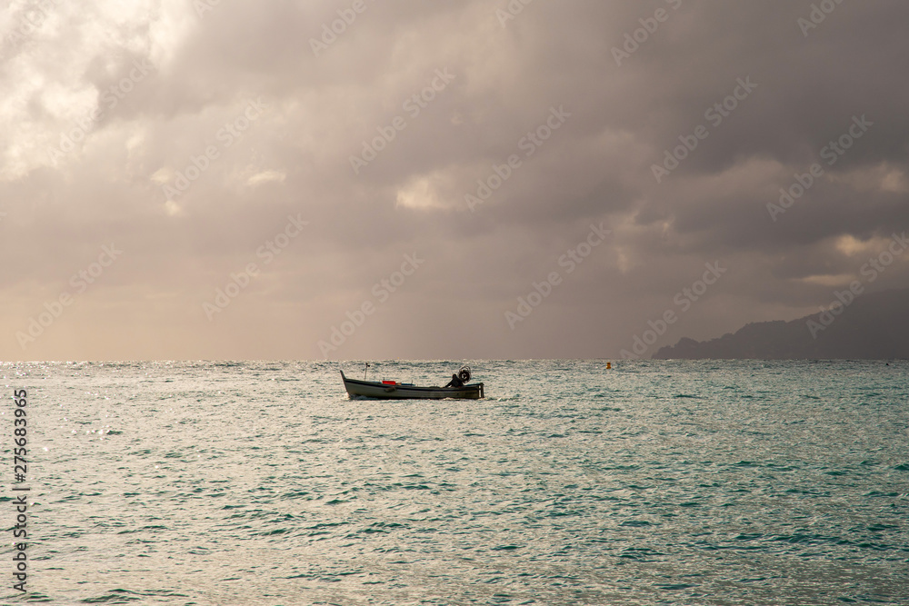 Backlight seascape of the Ligurian Sea with a fishing boat, a cape on the horizon in the background and cloudy sky, Sestri Levante, Genoa, Liguria, Italy Backlight seascape of the Ligurian Sea with a fishing boat, a cape on the horizon in the background and cloudy sky, Sestri Levante, Genoa, Liguria, Italy