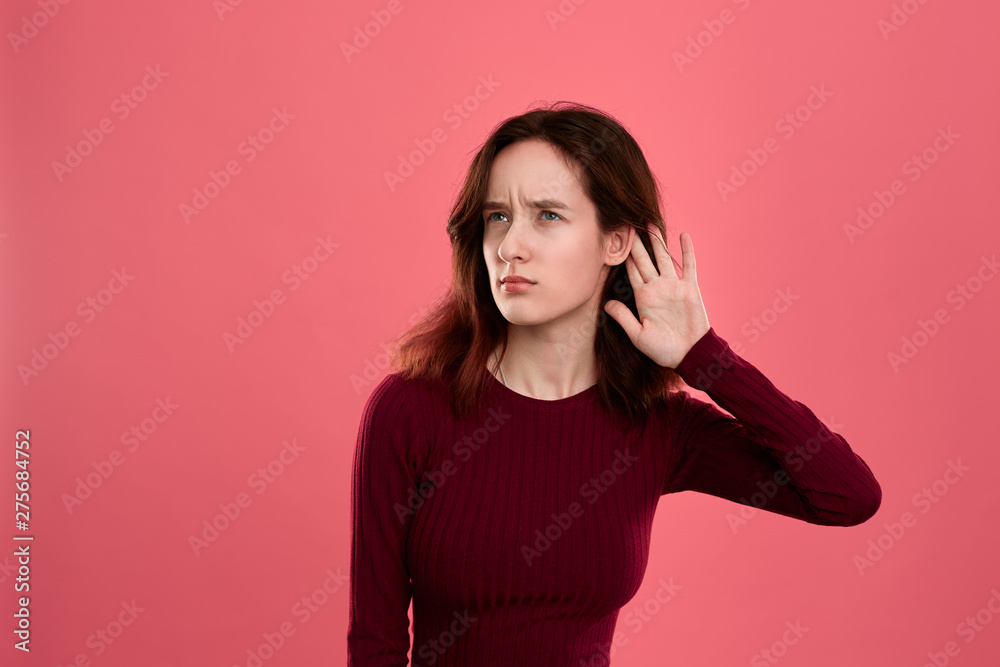 Surprised young lady standing isolated over dark pink background with hands raised close to ear as if is listening to some rumors. Surprised young lady standing isolated over dark pink background with hands raised close to ear as if is listening to some rumors.